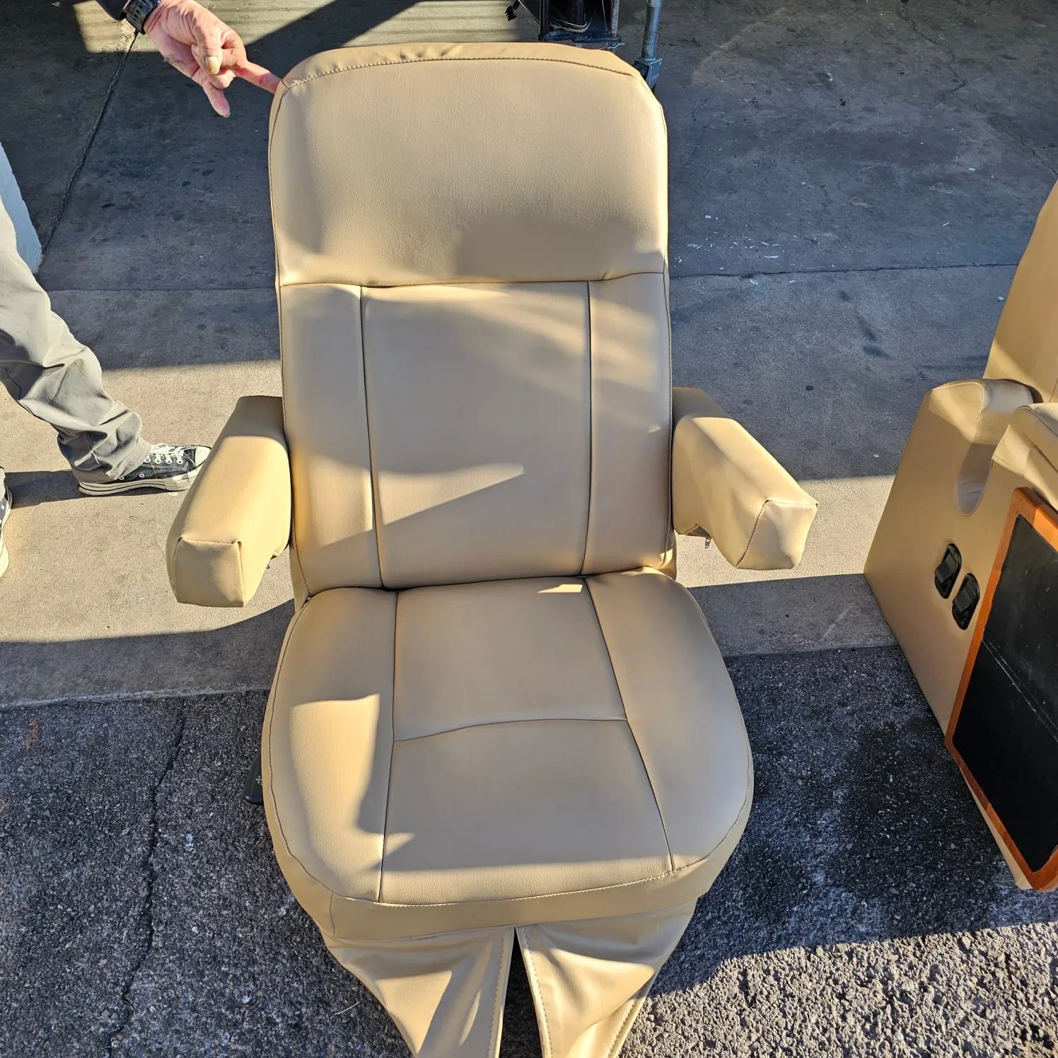 Man standing next to a tan leather boat seat on the ground, with a box beside it