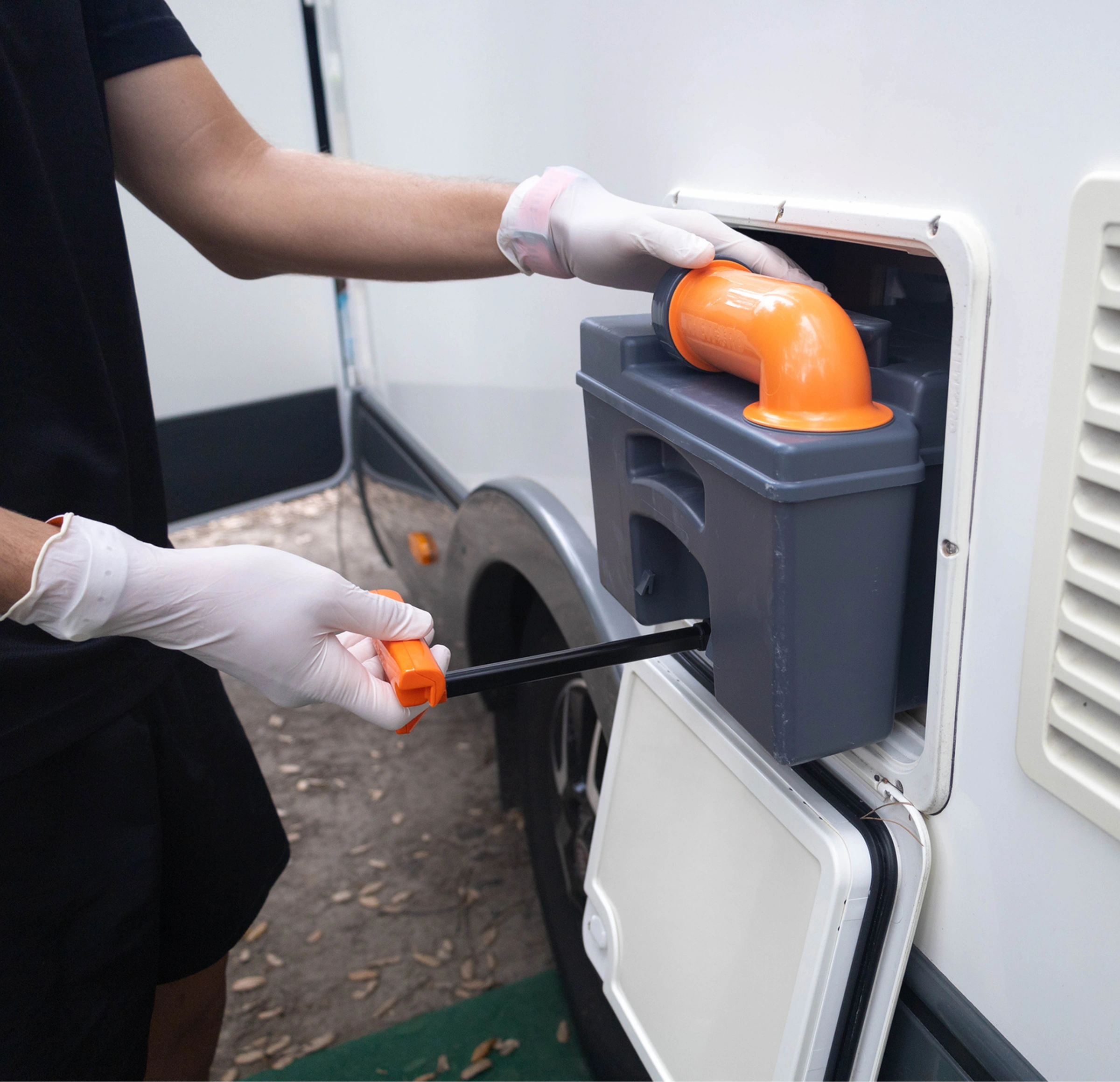 Person wearing white gloves and holding an orange object, likely a tool, while using a hose to clean a trailer